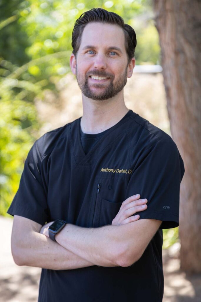 Dr. Anthony DeFont crossing his arms, standing outside, wearing a black scrubs with his name on it.