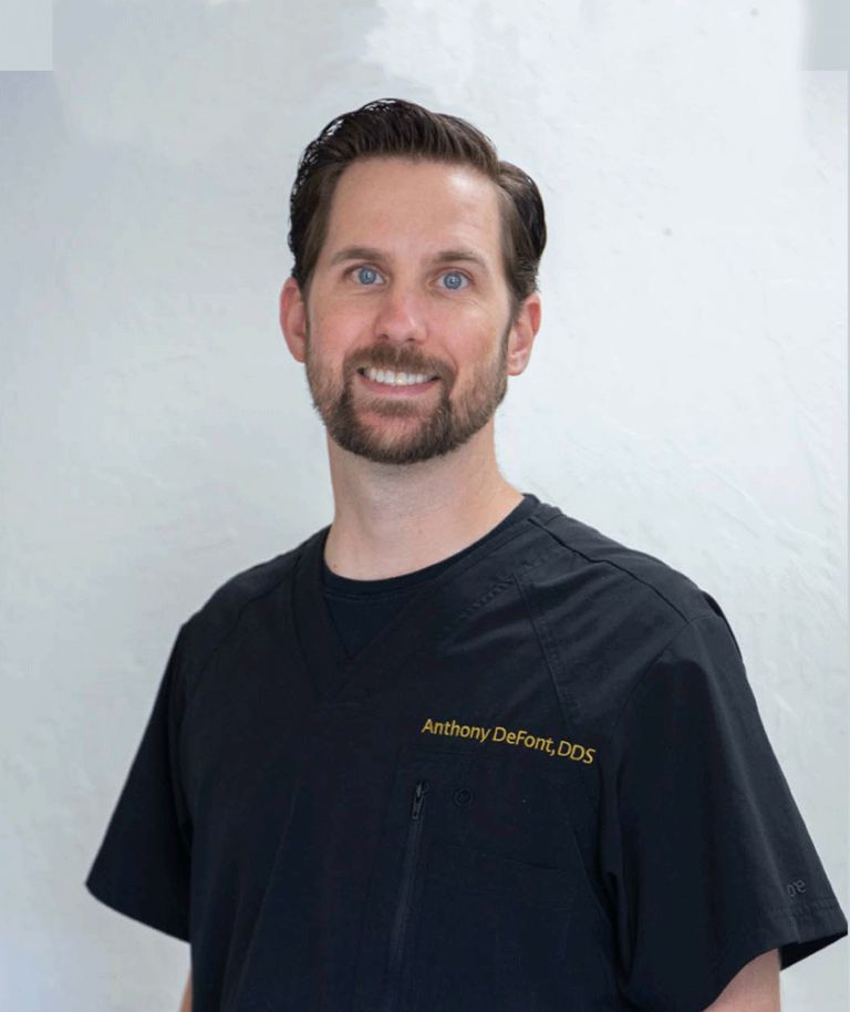 Dr. Anthony DeFont's name embroidered on a dark-colored scrub top, indicating the wearer is a dentist.